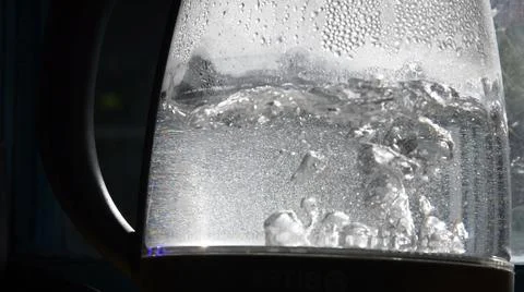 Blurry bubbles of boiling water in old transparent kettle at bright sunlight Stock Photos