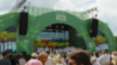 A blurry crowd faces a large green outdoor concert stage at an open-air fest Stock Footage 339909208