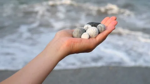 Blurry defocus Beautiful round gray and white sea stones lie in a female hand Stock Footage 134790354