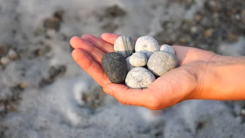 Blurry defocus Beautiful round gray, white sea stones lie in a female hand Stock Footage 134811888