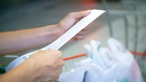 Blurry of hand of Asain man checking a bill with a long receipt in the supe.. Stock Photos