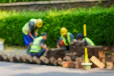 Blurry Image of Construction Workers Building a Roadside Brick Structure Outside Stock Photos