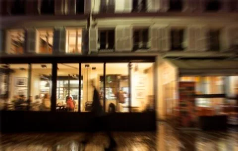 Blurry motion image of man walking in front of a restaurant at night in Paris Stock Photos