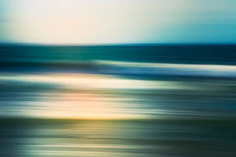 Blurry motion of ocean waves rolling toward the shore under a soft, cloudy sk Stock Photos