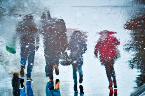 Blurry reflection in a puddle of four walking people on wet city street Stock Photos
