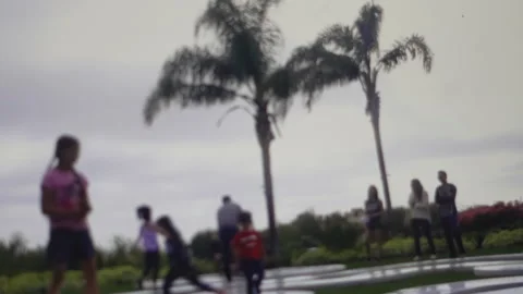 Blurry scene of children playing in a public park with palm trees and a cloudy Vídeos de archivo 342409747