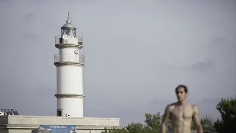 Blurry view of a young man approaching from a white lighthouse in slow-motion. Stock Footage 221737099