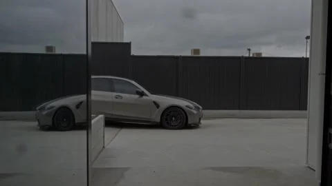 BMW M3 Pulls into Industrial Warehouse on Cloudy Day - Static Handheld Shot Stock Footage 304093294