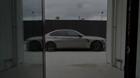 BMW M3 Pulls into Industrial Warehouse on Cloudy Day - Static Handheld Shot Stock Footage 304093308
