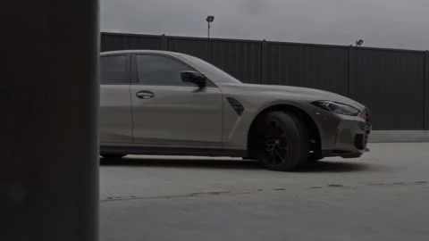 BMW M3 Pulls into Industrial Warehouse on Cloudy Day - Static Handheld Shot Stock Footage 304093386