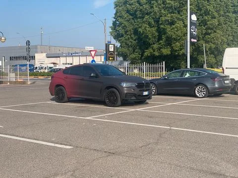 BMW X6 with custom matte red black gradient wrap parked beside a Tesla Mode.. Stock Photos