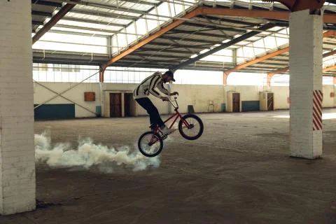 BMX rider in an empty warehouse using smoke grenade Fotos de archivo