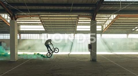 BMX rider in an empty warehouse using smoke grenade Stock Photos