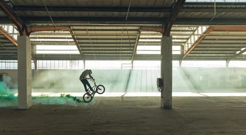 BMX rider in an empty warehouse using smoke grenade Stock Photos
