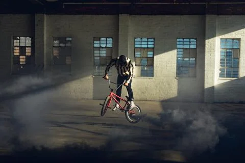 BMX rider in an empty warehouse using smoke grenade 스톡 사진