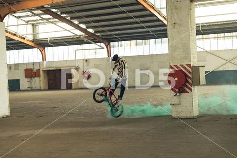 BMX rider in an empty warehouse using smoke grenade Stock Photos