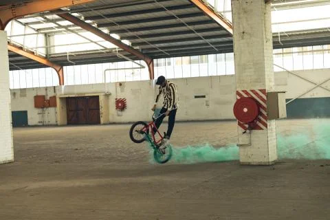 BMX rider in an empty warehouse using smoke grenade Stock Photos