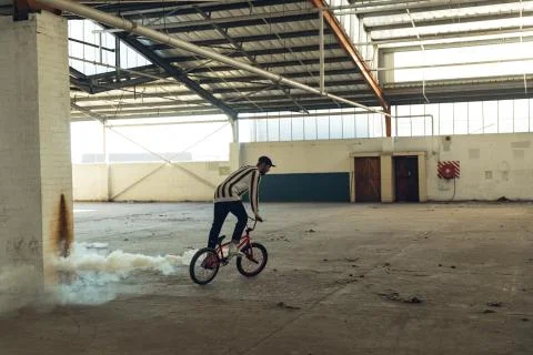 BMX rider in an empty warehouse using smoke grenade Stock Photos