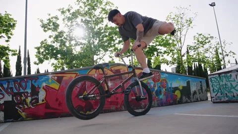 BMX rider performs flatland trick lifting leg while camera moves forward slow Stock Footage 336937133