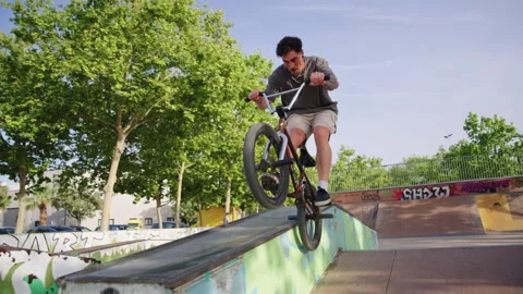 BMX rider performs trick on ledge and celebrates after landing at skatepark Stock Footage 336936393