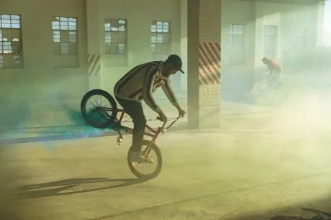BMX riders in an empty warehouse using smoke grenades Stockfoto's