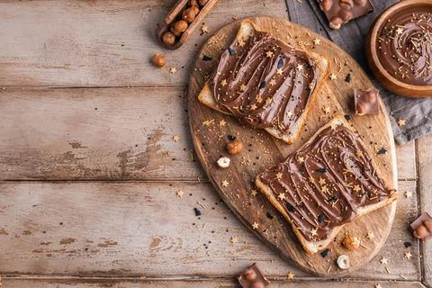 Board of bread with chocolate paste and hazelnuts on wooden background Stock Photos