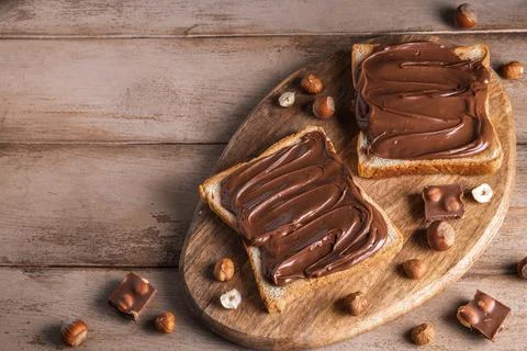 Board of bread with chocolate paste and hazelnuts on wooden background Stock Photos