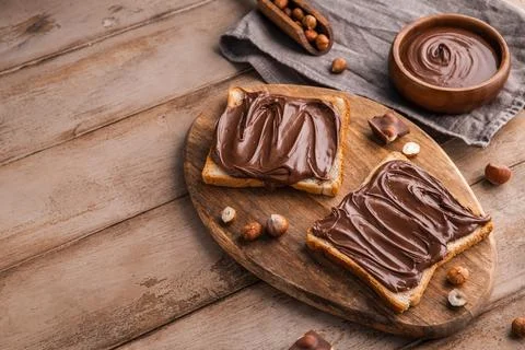 Board of bread with chocolate paste and hazelnuts on wooden background Stock Photos