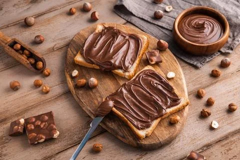 Board of bread with chocolate paste and hazelnuts on wooden background Foto stock