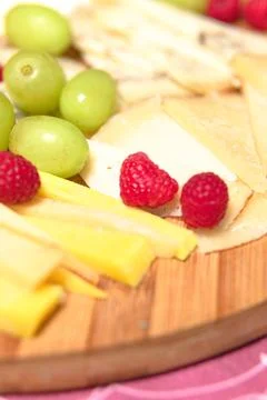 Board of different types of cheeses with raspberries and grapes. Stock Photos