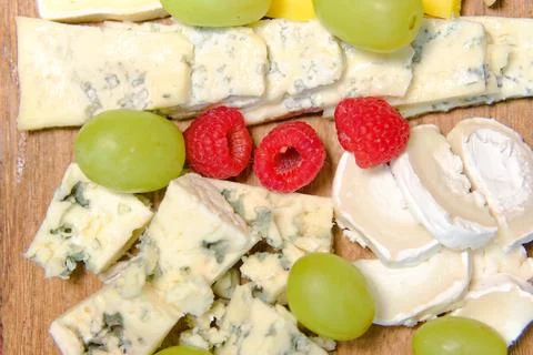 Board of different types of cheeses with raspberries and grapes. Stock Photos