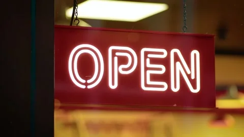 Board displaying open sign hanging inside brightly lit storefront. Panel showing Stock Footage 318901532