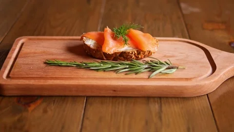 On the board lies a slice of bread topped with red fish. This savory morsel Stock Footage 265573708