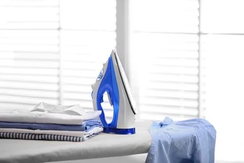 Board with modern iron and stack of clothes indoors, space for text. Laundry  Foto stock