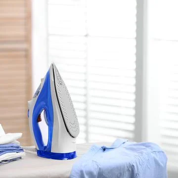 Board with modern iron and stack of clothes indoors, space for text. Laundry  写真素材