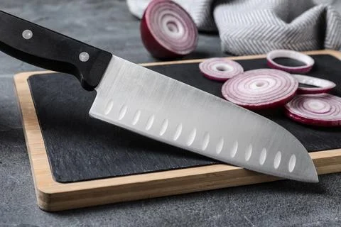 Board with sharp knife and cut onion on grey background Foto stock