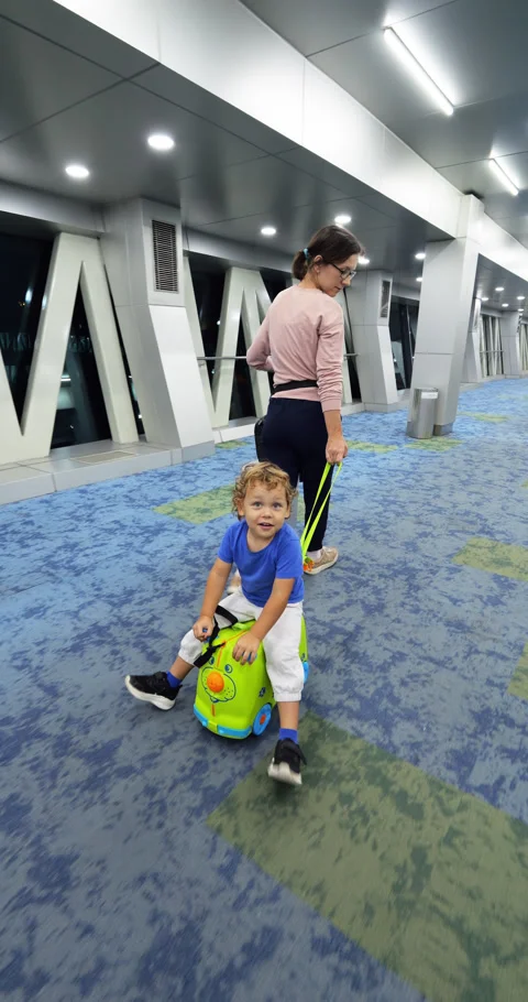 Boarding time, mom pulling toddler son sitting backwards on ride-on suitcase Stock Footage 284707235