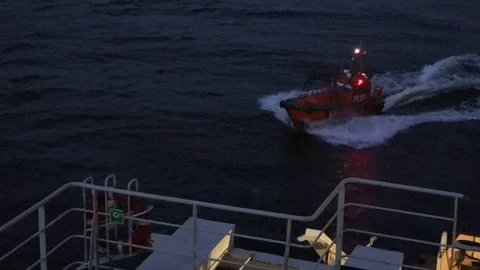 Boat with bright flashlights chases large ship sailing fast Stock Footage 113093539