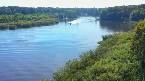 A boat cruises on a tranquil lake, surrounded by forest. Stockbeeldmateriaal 312167366