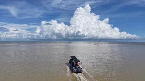 Boat cuts through calm, murky water under vast, puffy clouds Stock Footage 338996544
