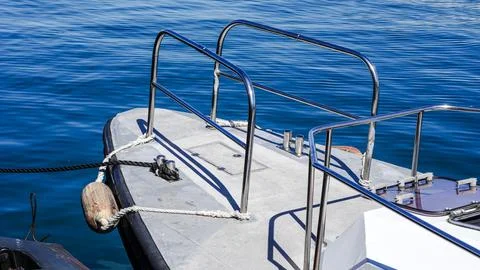 Boat deck with railing and mooring line on calm blue water surface Stock Photos