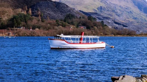 Boat floating gently on a lake surrounded by mountains zooming and panning out Stock Footage 104751375