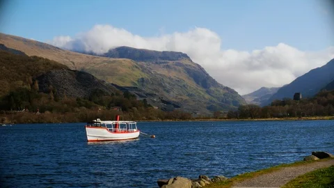 Boat floating gently on a lake surrounded by mountains, UHD Stock Footage 104752111