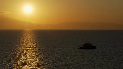 A boat is floating on the sea with the sun setting in the background Stock Footage 320002364