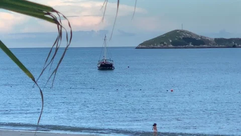 Boat floats in ocean close to beach with island in the back Stock Footage 112361460