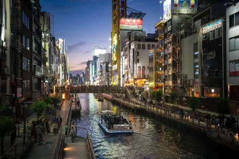 A boat is gliding down a winding river through Osaka city during nighttime Stock Photos