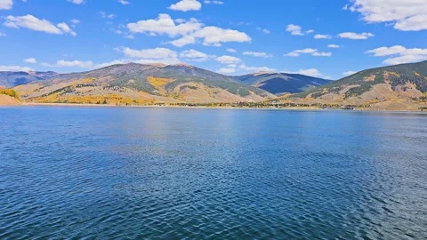 Boat level view across a calm mountain lake, with blue water, golden autumn Stock Footage 344904445