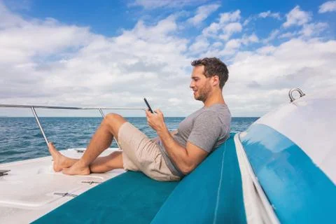 Boat man using mobile phone texting on satellite internet while relaxing on deck Stock Photos