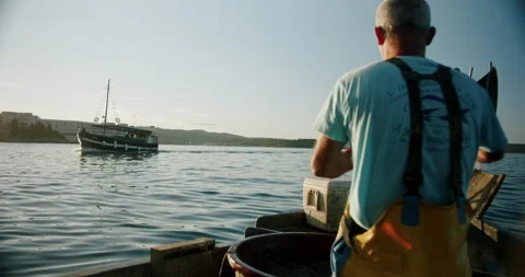 Boat passing by fisherman while pulling his net out of the sea water Stock Footage 161184274