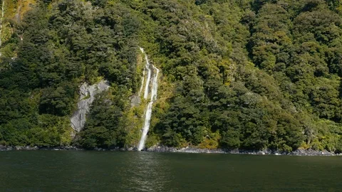 Boat passing small waterfall surrounded by green trees at Milford Sound. Vídeos de archivo 90365363